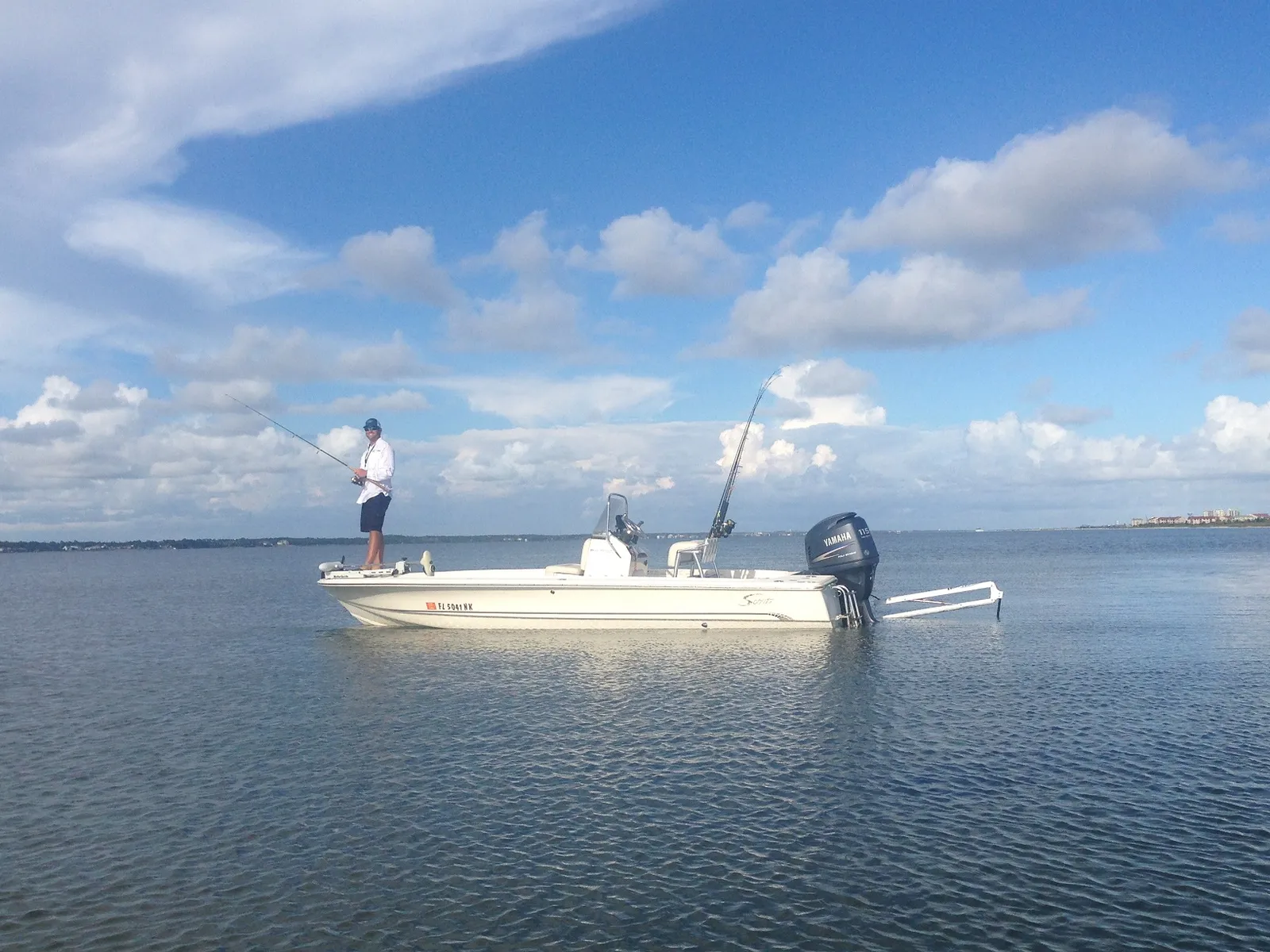 Angler casting from the bow of a white flats boat on calm water