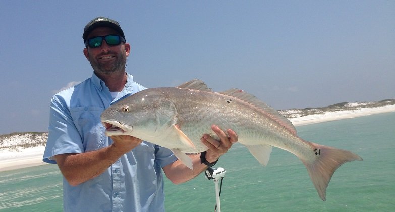 Captain Mike holding a large redfish with white sand beach behind