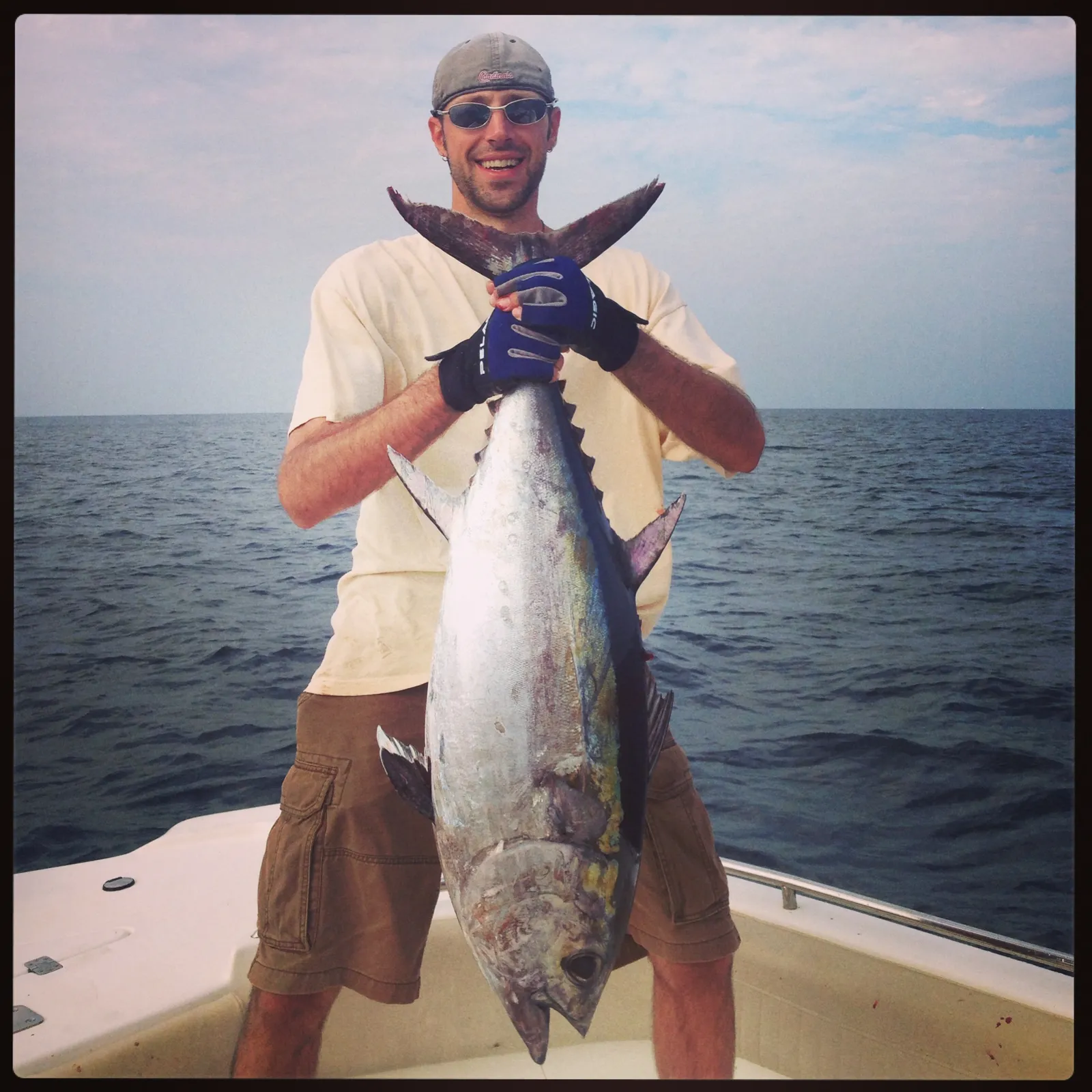 A smiling angler holding a big tuna on the boat with open water behind
